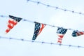 Flags with American colors with red stripes and white stars on blue background hanging in a row surrounded by a barbed wire