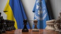 Flags of Ukraine and United Nationsbehind pawns on the chessboard. Political rivalry related 3D rendering