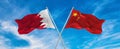 flags of China and Bahrain waving in the wind on flagpoles against sky with clouds on sunny day. Symbolizing relationship, dialog