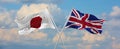 flags of Japan and Great Britan waving in the wind on flagpoles against sky with clouds on sunny day. Symbolizing relationship,