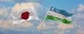flags of Japan and Uzbekistan waving in the wind on flagpoles against sky with clouds on sunny day. Symbolizing relationship,