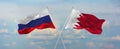 flags of Russia and Bahrain waving in the wind on flagpoles against sky with clouds on sunny day. Symbolizing relationship, dialog