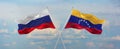 flags of Russia and Venezuela waving in the wind on flagpoles against sky with clouds on sunny day. Symbolizing relationship,