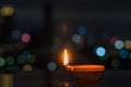 The flame of clay diya lamp with colorful city bokeh lights.
