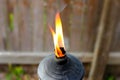Flame from metal Tiki torch against blurred wooden fence Royalty Free Stock Photo