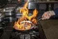 Flame in the pan. Professional Chef makes flambe for food in the restaurant kitchen. Chef cooking with open fire pan on a stove Royalty Free Stock Photo