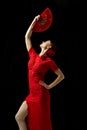 Flamenco female dancer in ornate red dress standing with elegance, posing with red fan against black background Royalty Free Stock Photo