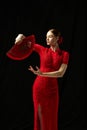 Flamenco female dancer in ornate red dress standing with elegance, posing with red fan against black background Royalty Free Stock Photo