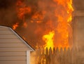 Flames Blazing from a backyard fire with the fence and house on fire.