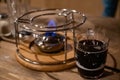 Transparent glass mug with hot mulled wine inside near metal burner for traditional French cheese fondue. Blue flaming fire Royalty Free Stock Photo