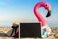 Flamingo print. Pink inflatable flamingo with black desk, slippers and hat for text on summer sea beach background in sunny day. Royalty Free Stock Photo