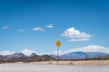 A flash flood area warning sign along an empty road in the desert  with mountains and plants under a blue sky with clouds Royalty Free Stock Photo