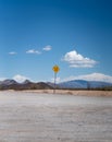 A flash flood area warning sign along an empty road in the desert  with mountains and plants under a blue sky with clouds Royalty Free Stock Photo