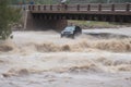 flash flood rushing past bridge, with vehicles and people at risk of being swept away