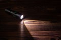 Flashlight and a beam of light in darkness. A modern led lamp with bright projection on dark wood table Royalty Free Stock Photo