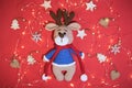 Flat background for new year or Christmas. Charming hand knitted amigurumi deer in blue sweater and red scarf on red background Royalty Free Stock Photo