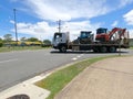 flat bed truck carrying a bobcat and excavator construction vehicles