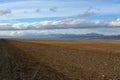 Flat boundless steppe with yellowed grass at the foot of a high mountain range under a cloudy autumn sky in the early evening Royalty Free Stock Photo