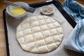 Flat bread dough with the typical pattern for Turkish Ramadan pide on a baking tray with paper, egg yolk for coating and sesame