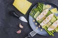 Flat with copy space. On a black plate are green asparagus, sliced turkey with peanut sauce and parmesan cheese. A