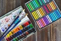 Flat lay art workplace, wooden table with paint brushes, watercolor paints and crayon pastel chalks close up. Copy space