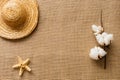 Flat lay background with starfish, straw hat and cotton flower on burlap fabric/summer beach vacation concept