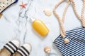 Flat lay beach accessories. Sunscreen cream bottle, striped beach bag and female sandals, seashells on marble background. Concept Royalty Free Stock Photo