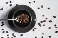 Flat lay beverage background of roasted coffee beans in spoon over a cup of coffee on white marble background with roasted coffee