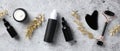 Flat lay black obsidian face roller, gua sha, serum, essential oils and golden branches on stone table. Luxury skincare cosmetics