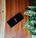 Flat lay of a black phone over a wood background and some leaves near it with the word inspire written in it