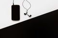 Flat lay with black smartphone connects to black earphones on white and black background. Top view on personal accessories Royalty Free Stock Photo