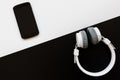 Flat lay with black smartphone on white and white headphones on black background. Top view on personal accessories