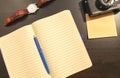 Flat lay of blank page of opened notebook, blue pen, mechanical watches with brown band, old film camera and photo envelop