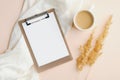 Flat lay blank paper clipboard, cup of coffee, white blanket and dry flowers on beige background. Top view home office desk table Royalty Free Stock Photo