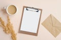 Flat lay blank paper clipboard, envelope, cup of coffee and dry flowers on beige background. Top view home office desk table, Royalty Free Stock Photo