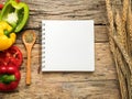 Flat lay of blank recipe cooking book and utensils with herbs and colorful bell pepper over wooden background. top view