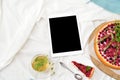 Flat lay breakfast in bed with raspberry cheesecake, mint tea and open note book, tablet
