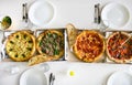 Flat lay of cardboard boxes with a variety of freshly baked delicious pizza on a served table with a white tablecloth. Italian