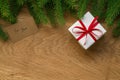 Flat lay christmas background with spruce twigs and white gift box with red ribbon on oak wood surface Royalty Free Stock Photo