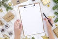 Flat lay christmas clipboard mockup. Woman`s hands holds black brush pen. Blank white paper sheet clip board mock up