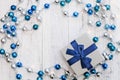 Flat lay Christmas gift with blue ribbon and silver and blue Christmas balls and garland on white wooden background Royalty Free Stock Photo