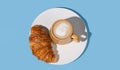 Flat lay of coffee cup and fresh croissant on a white plate on a blue background Royalty Free Stock Photo