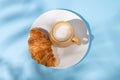 Flat lay of coffee cup and fresh croissant on a white plate on a blue background with shadow Royalty Free Stock Photo