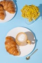 Flat lay of coffee cup and fresh croissants on blue background with yellow flowers and shadow Royalty Free Stock Photo