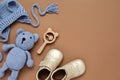 Flat lay composition with baby accessories set: crib shoes, teddy bear toy, knitted hat, wooden rattle and copy space.