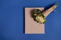 Flat lay composition of a beautiful bouquet of asters in craft paper on a beige notebook, lying on a blue background with space