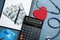 Flat lay composition with calculator, money and red heart on wooden surface. Health insurance concept Royalty Free Stock Photo