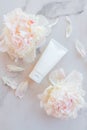 Flat lay composition with cosmetic products and peony flowers on a marble. Top view. Unbranded plastic white tube with face or