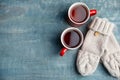 Flat lay composition cups of hot tea and knitted mittens on blue wooden background. Winter drink