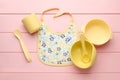Flat lay composition with drool baby bib and plastic dishware on pink wooden background